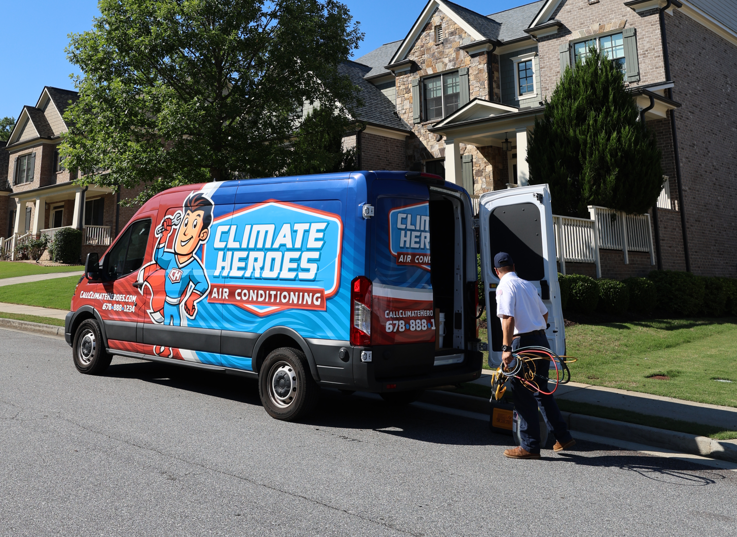 Climate Heroes HVAC technician carrying diagnostic gauges from a branded service van in a customer's driveway