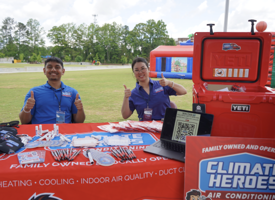 Climate Heroes team members giving a thumbs up at an event booth featuring a red Yeti cooler giveaway and branded merchandise
